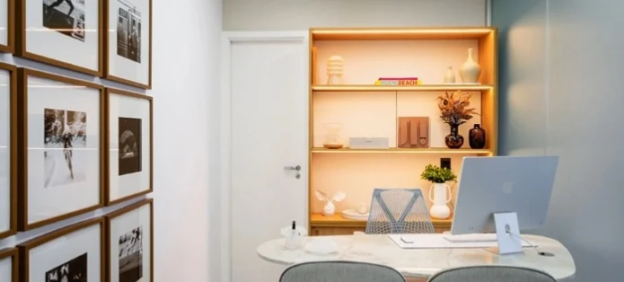 Vista do consultório com mesa de atendimento, quadros e estante iluminada.