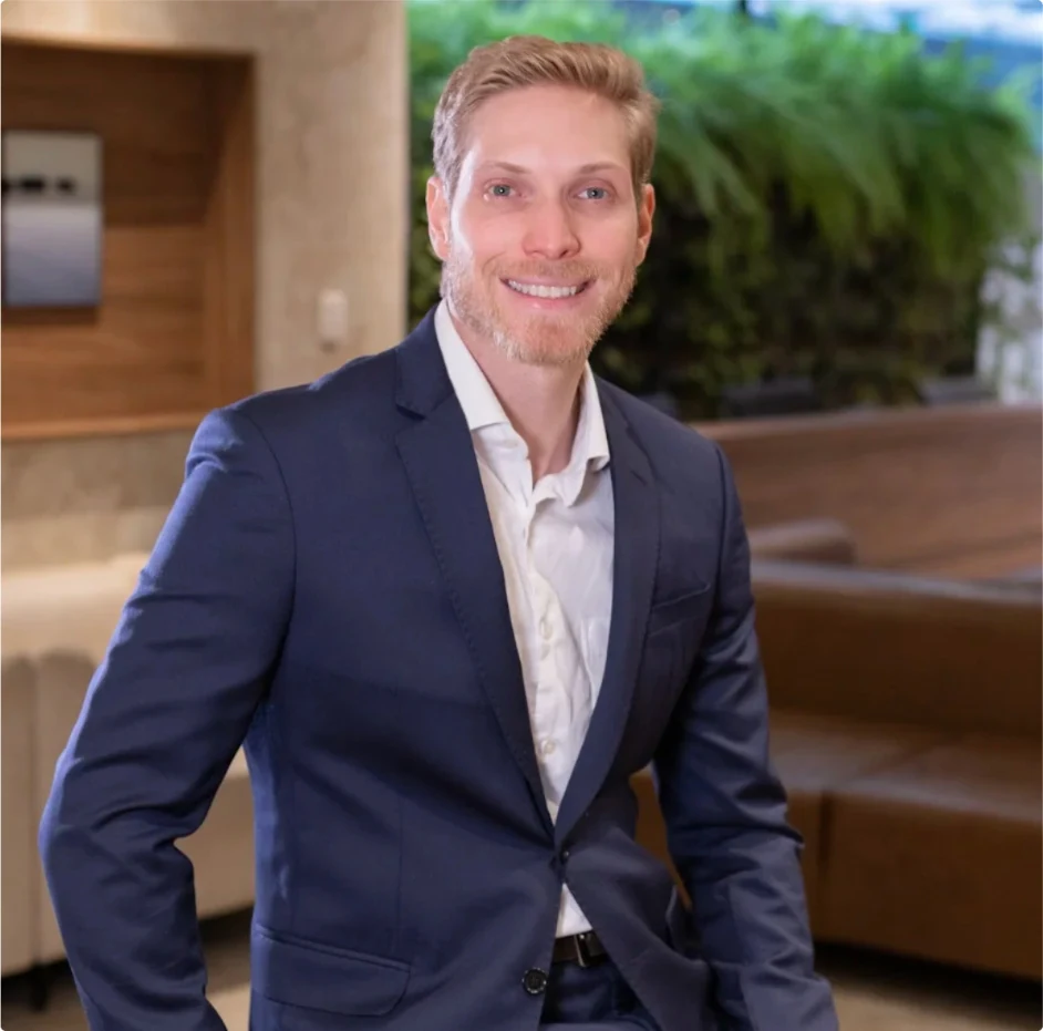 Dr. Stefano Cogo Badan, de terno azul e camisa branca, em um ambiente com vegetação ao fundo.
